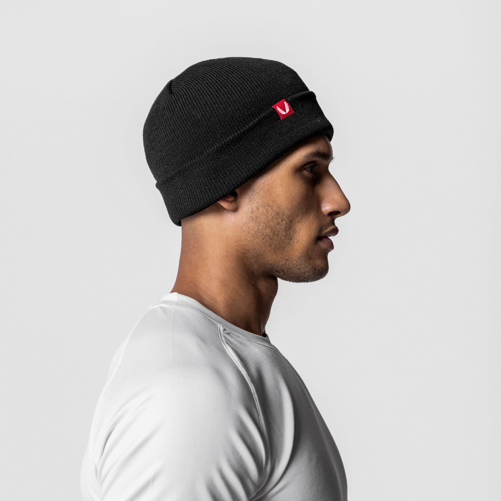 Essential Beanie in black with red logo patch, worn by model in profile view