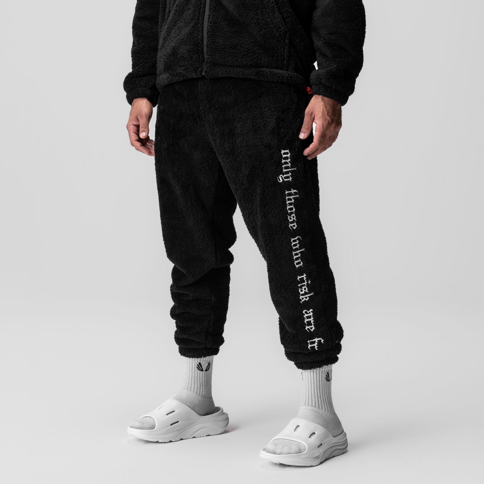 Black sherpa recovery sweats with white text on leg, worn with white socks and slides