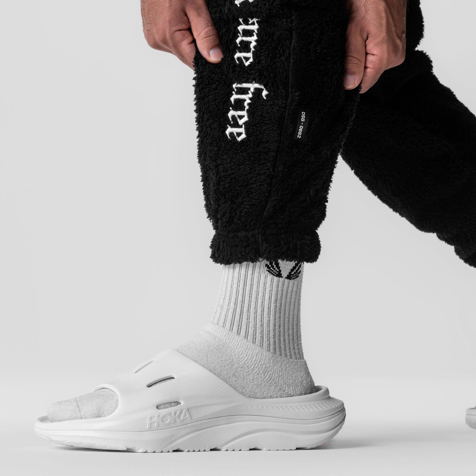 Sherpa Recovery Sweats in black worn with white socks and white slide shoes, lower body detail shot