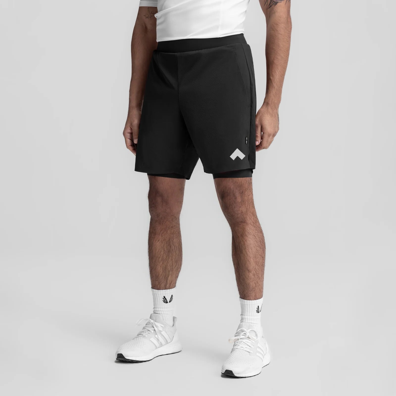 Black 7" liner shorts with white chevron logo, modeled with white sneakers and socks