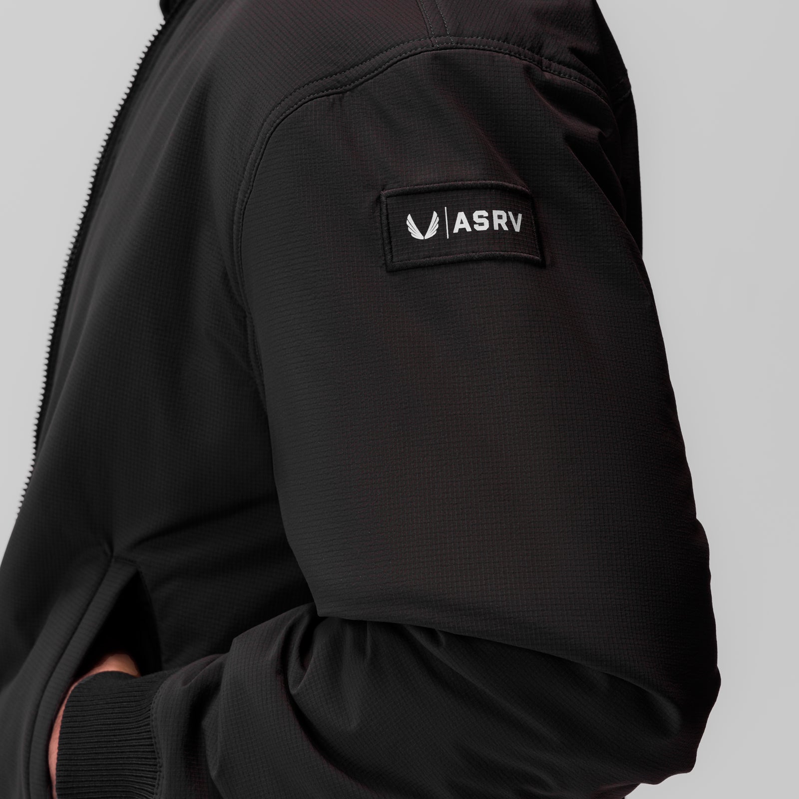 Black ripstop insulated bomber jacket worn by model, showing ASRV brand label on sleeve
