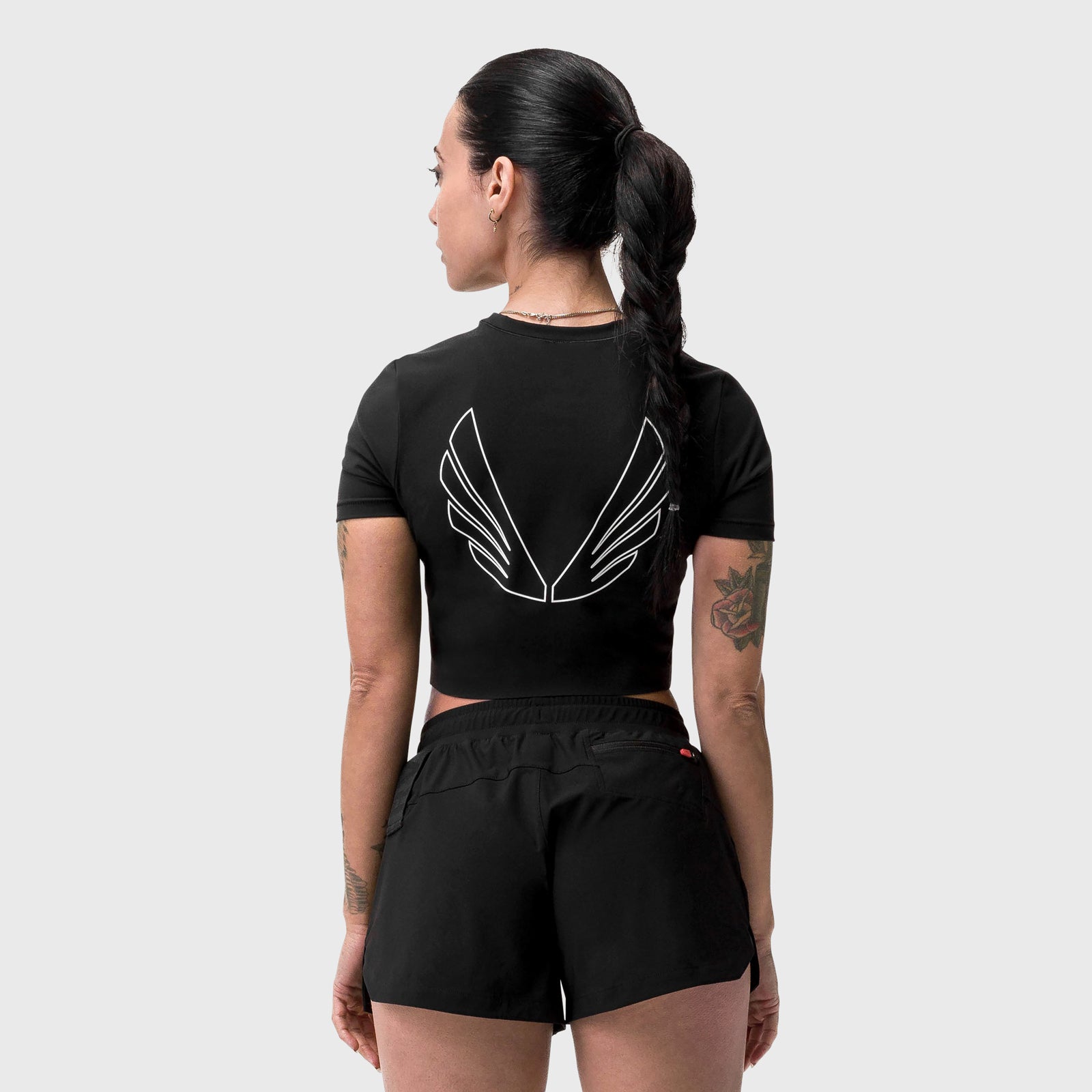 Black cropped tee with white wing graphic on back, worn by model, rear view