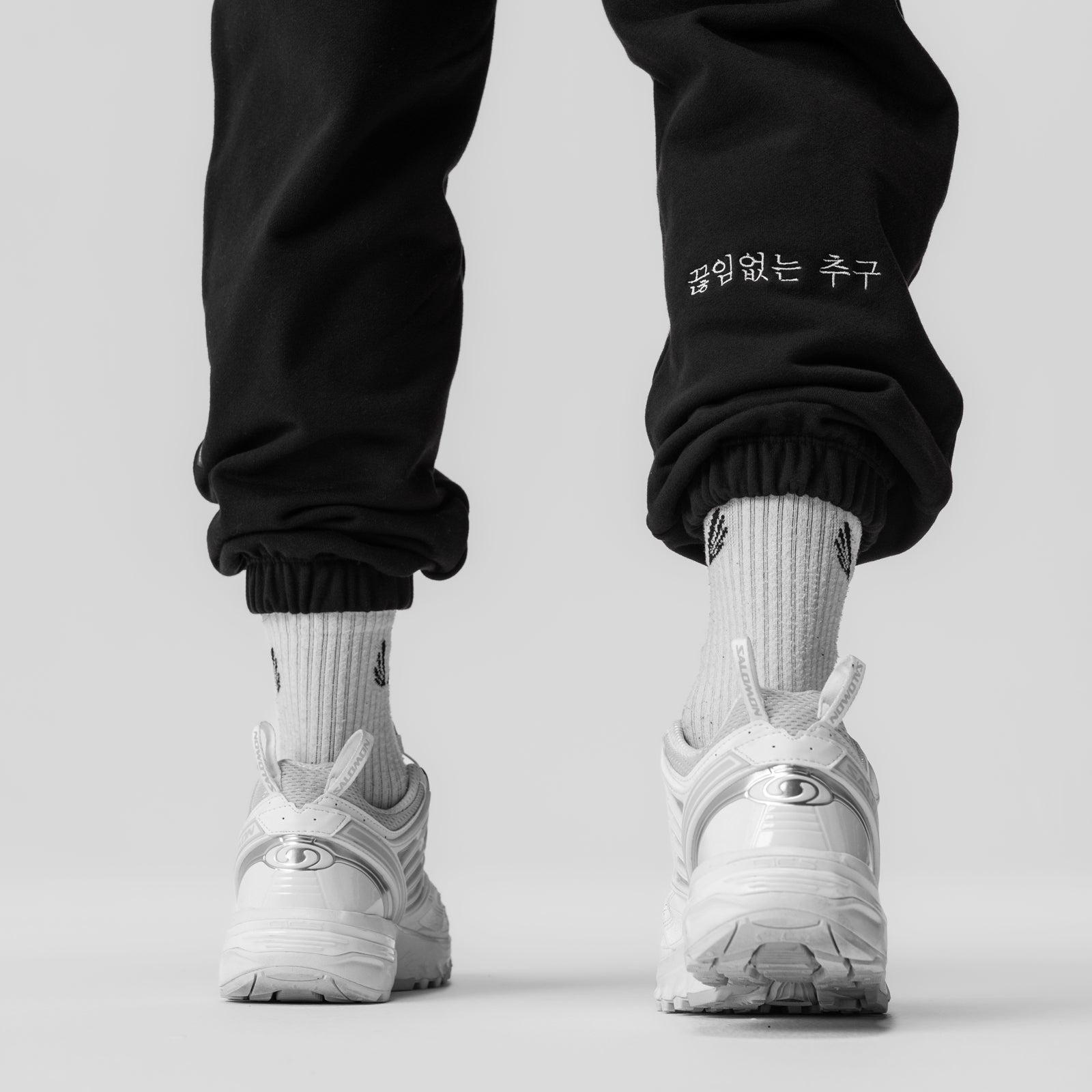 Black Tech-Terry oversized sweats with Korean text embroidered on cuff, worn with white socks and sneakers, back view