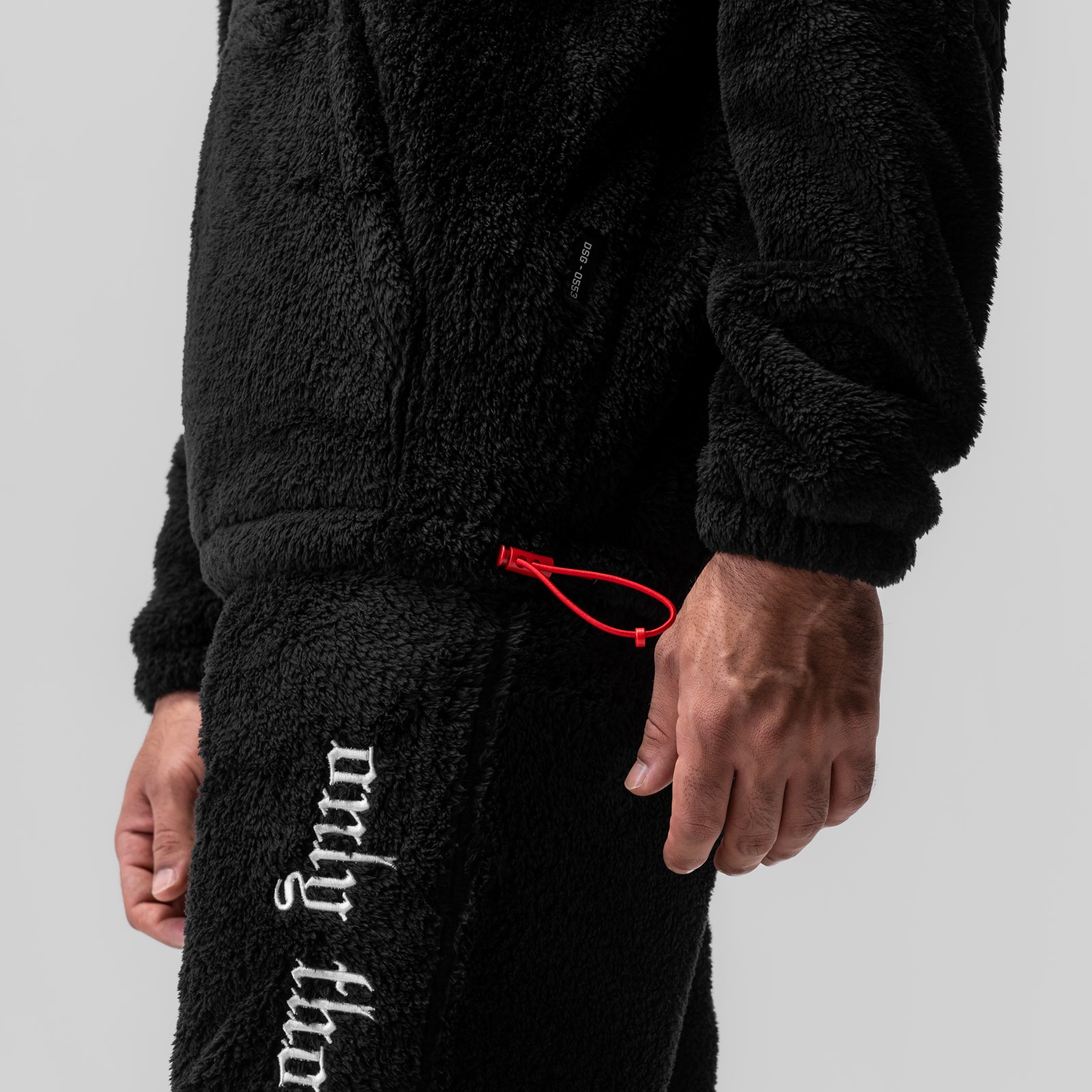 Black sherpa recovery hoodie worn by model, side view showing white text detail and red drawstring