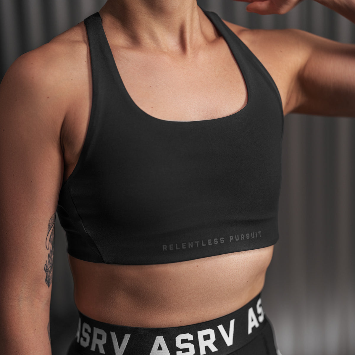 Black Lycra hybrid sports bra worn by model, front view showing "Relentless Pursuit" text