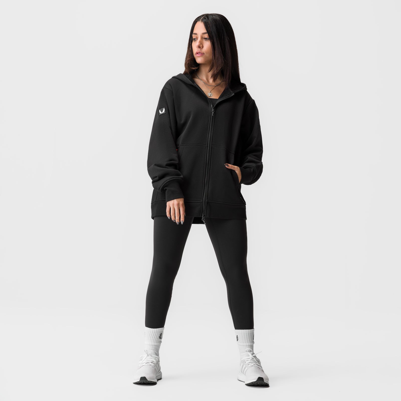 Black oversized zip hoodie worn by model with black leggings and white socks, front view