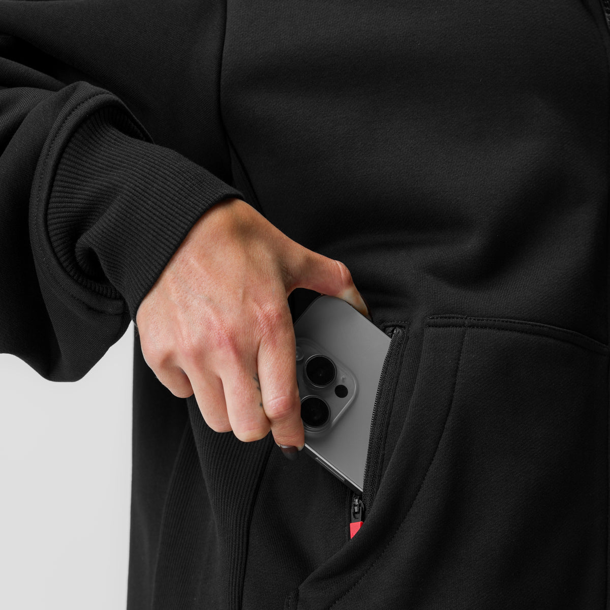 Black oversized zip hoodie worn by model holding phone in pocket, side view