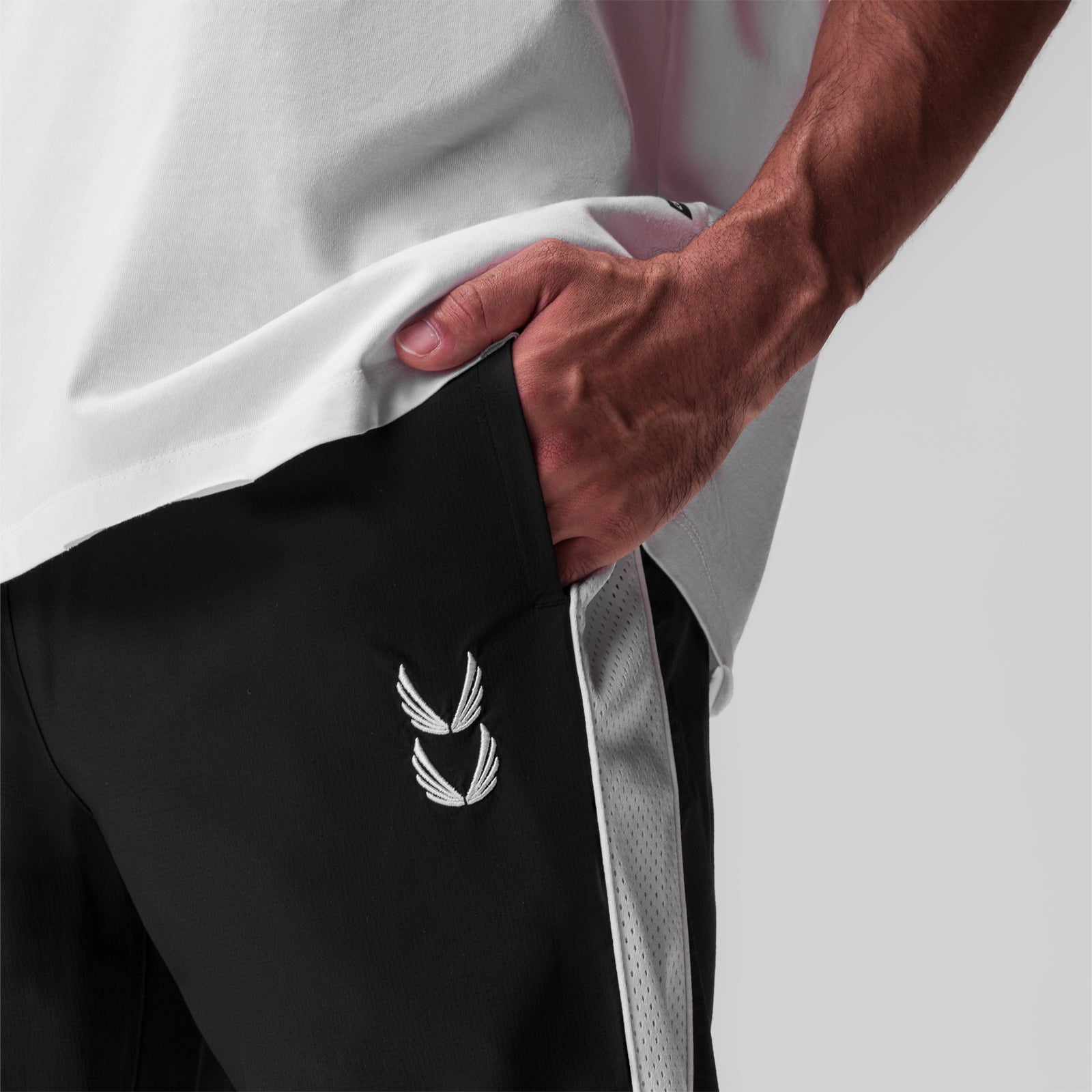 Black ripstop oversized track pant worn by model, detail shot of pocket with winged logo