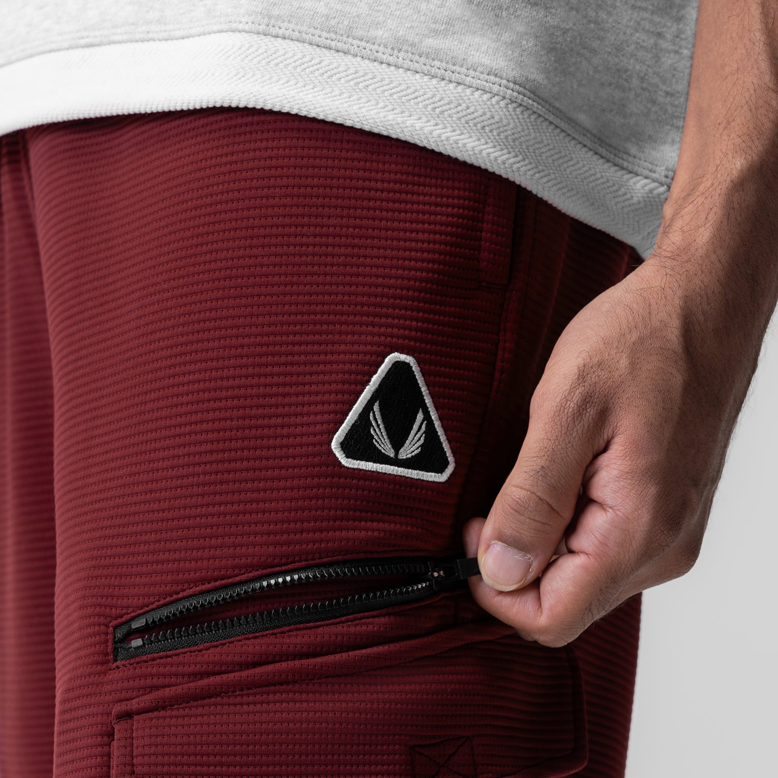 Deltapeak Cargo Cinch Jogger in crimson, modeled with hand showing zipper pocket detail