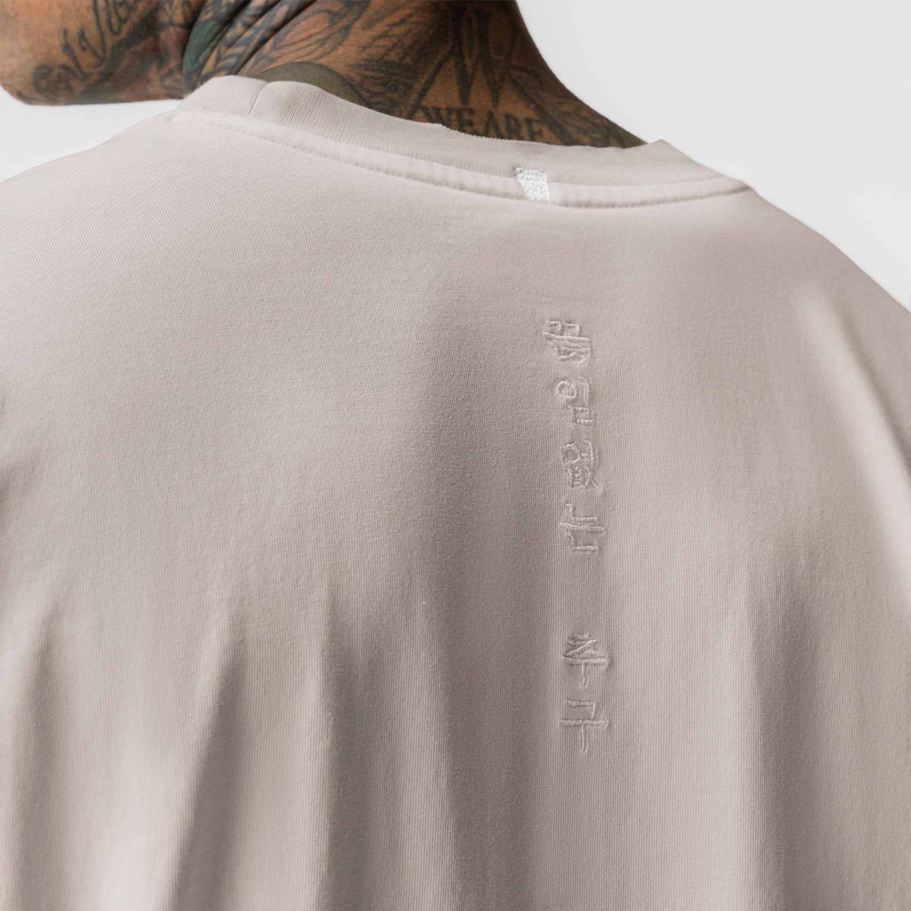 Tech Essential Relaxed Long Sleeve in Faded Chai, back view on model showing embroidered text detail