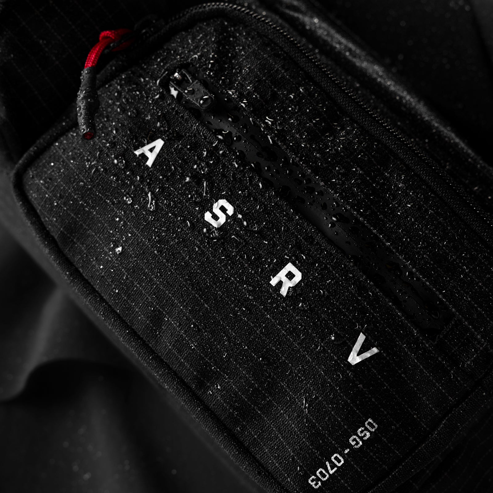 0703 Cordura Tech Crossbody Pack in black grid, carried with red zipper pull visible