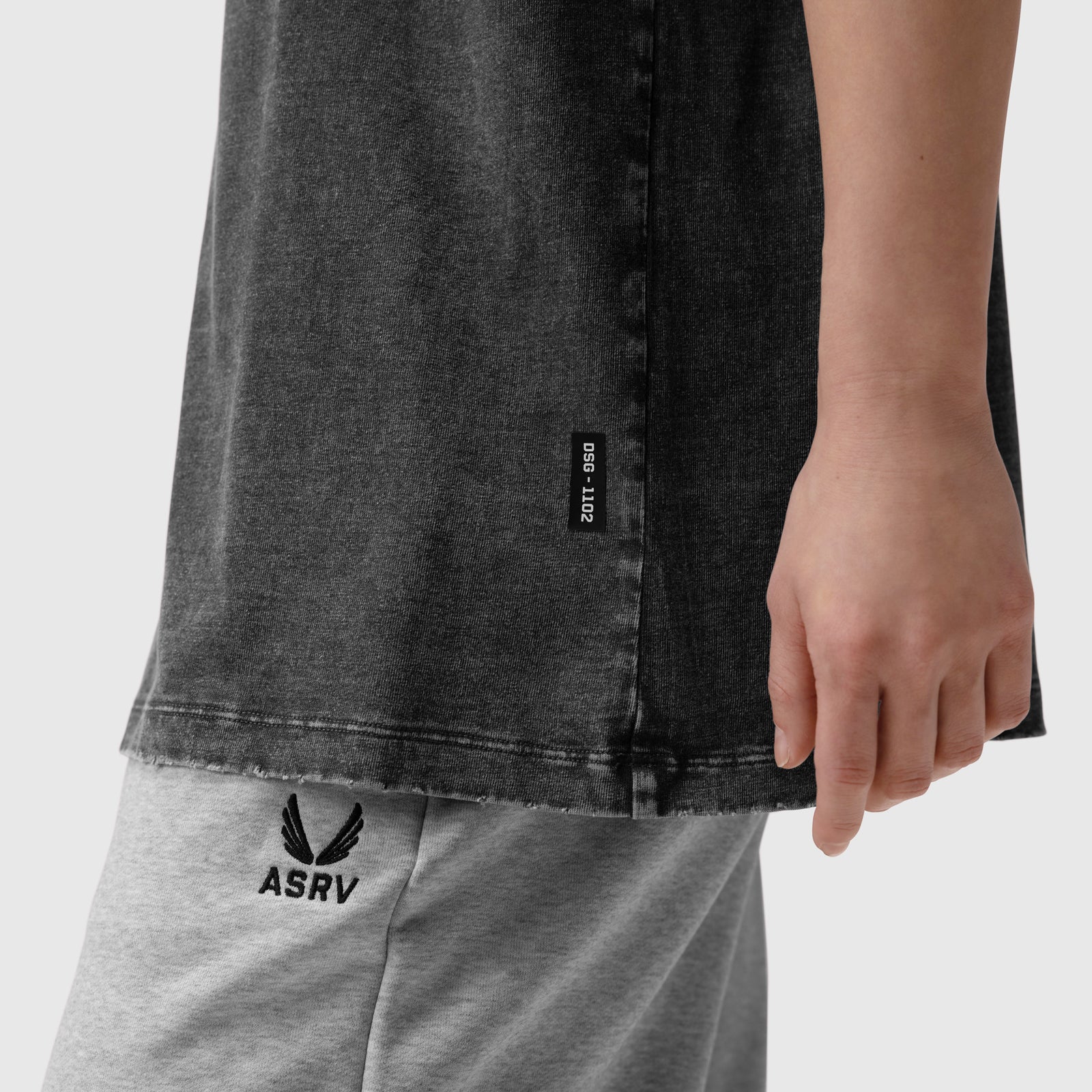 Distressed Relaxed Tee in black worn with grey joggers, detail shot of side seam and ASRV logo