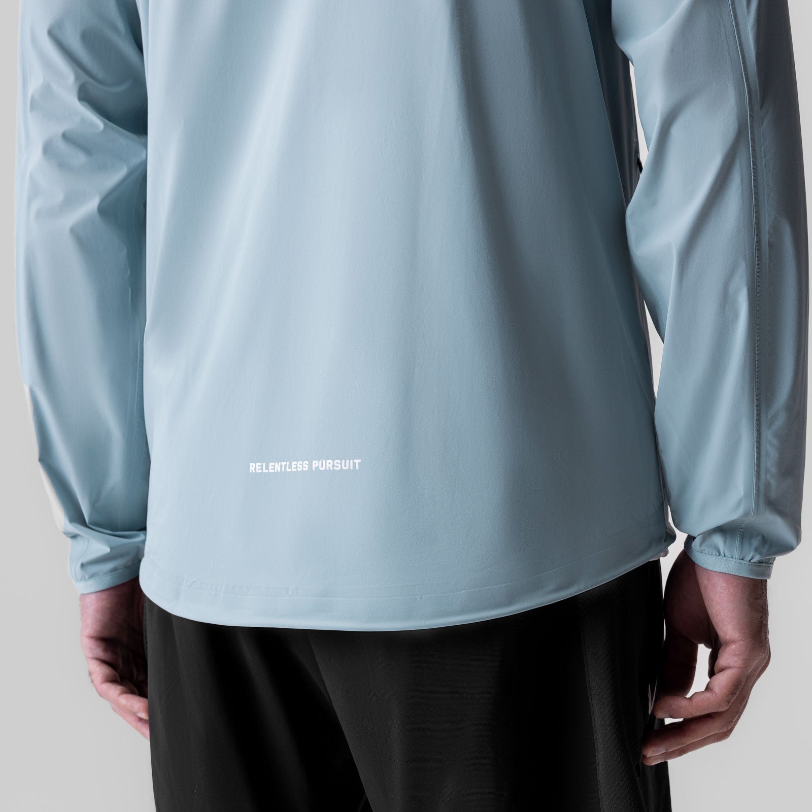 Aerotex Lightweight Windbreaker in light sky worn by model, back view showing 'Relentless Pursuit' text