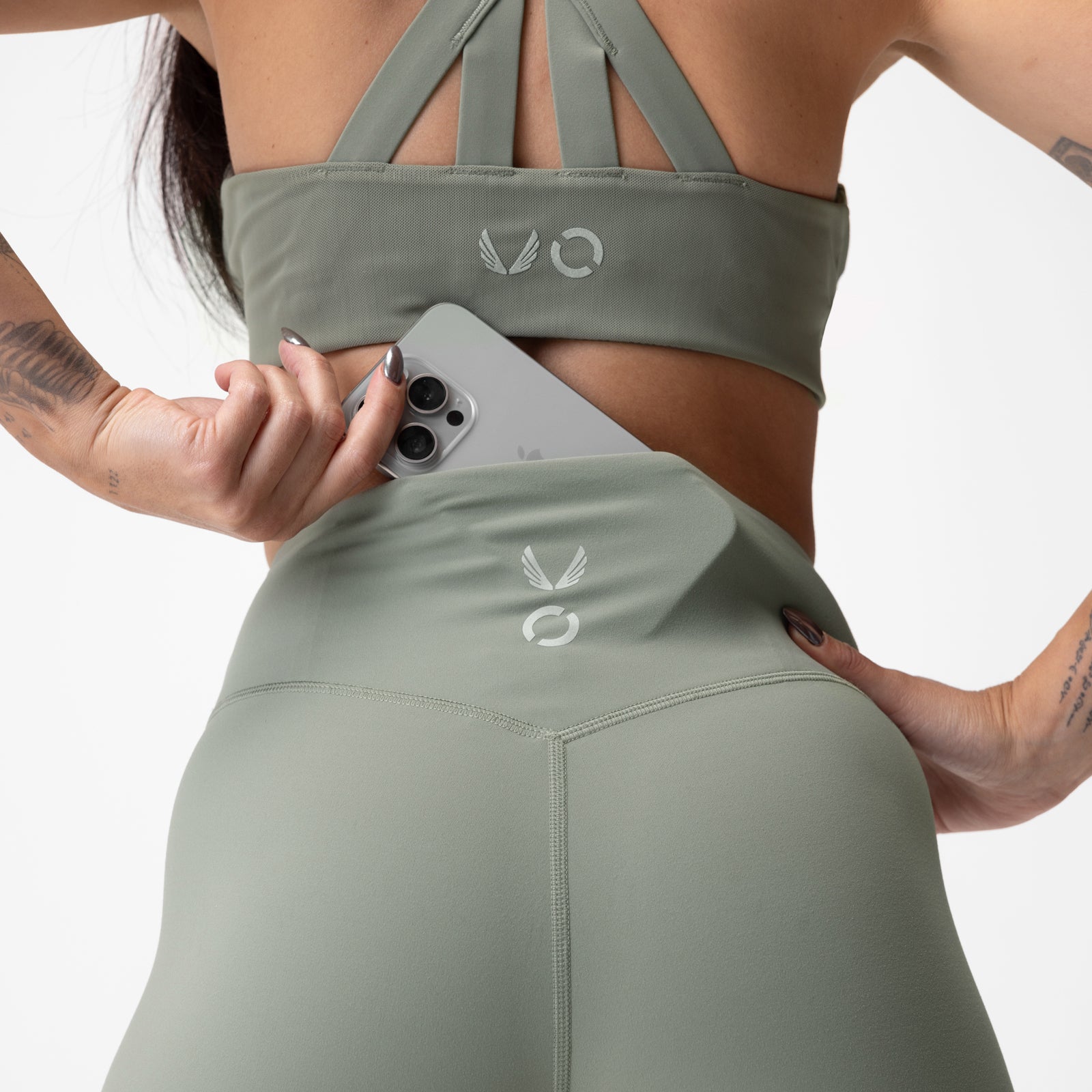 Sage green Lycra 7/8 leggings modeled from behind, holding phone at side
