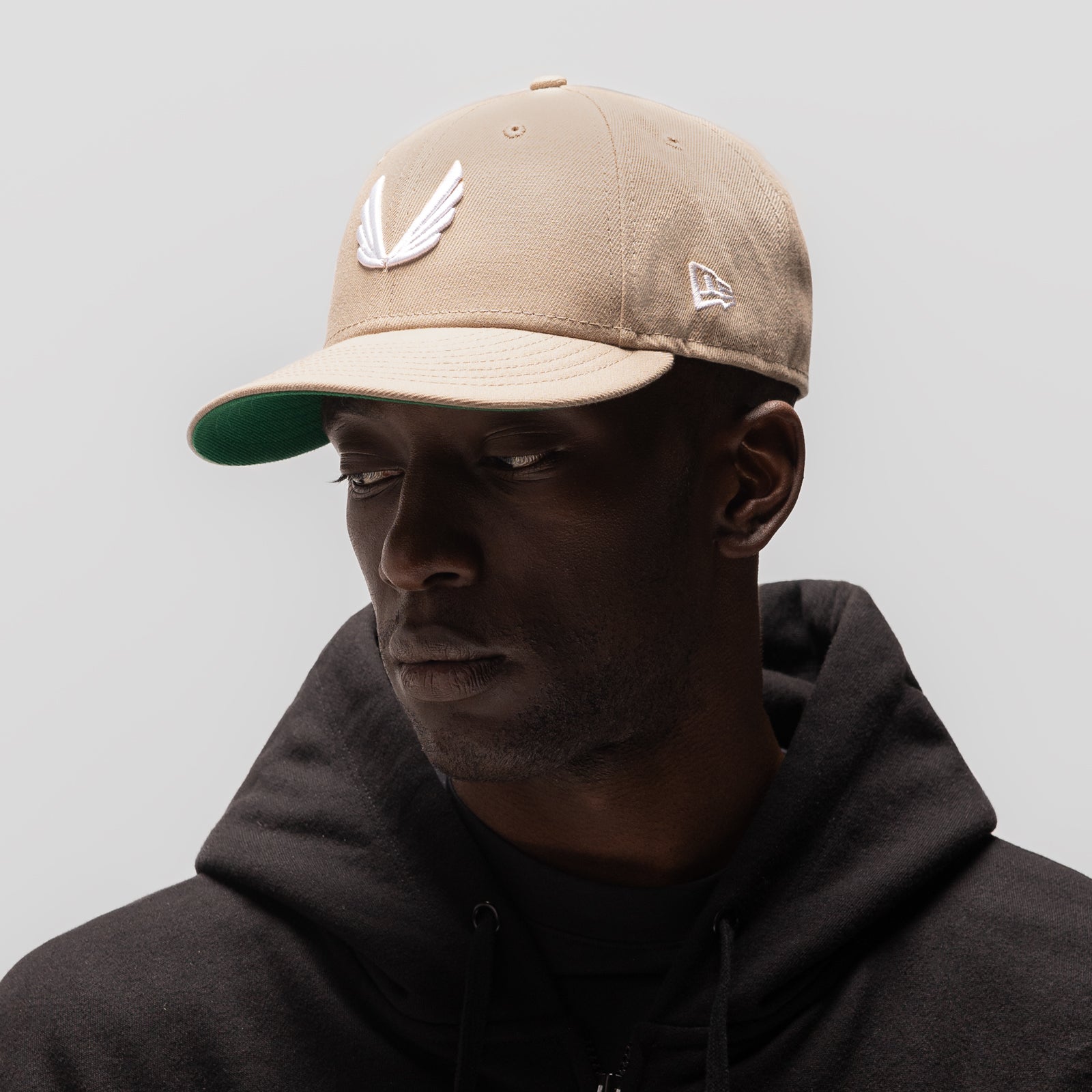 Beige and white New Era 59Fifty hat with wings logo, worn by model, side profile view
