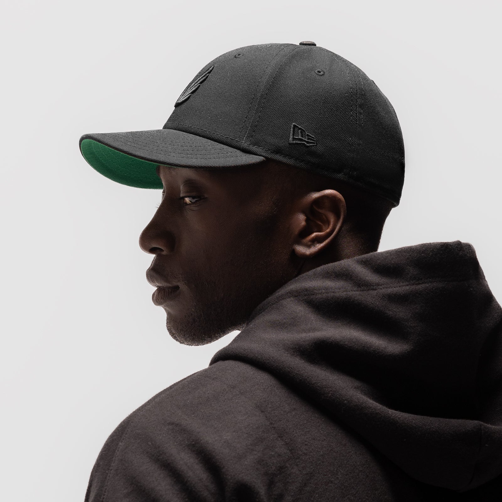 New Era 59Fifty Low Profile Hat in black with green undervisor, worn by model in profile view