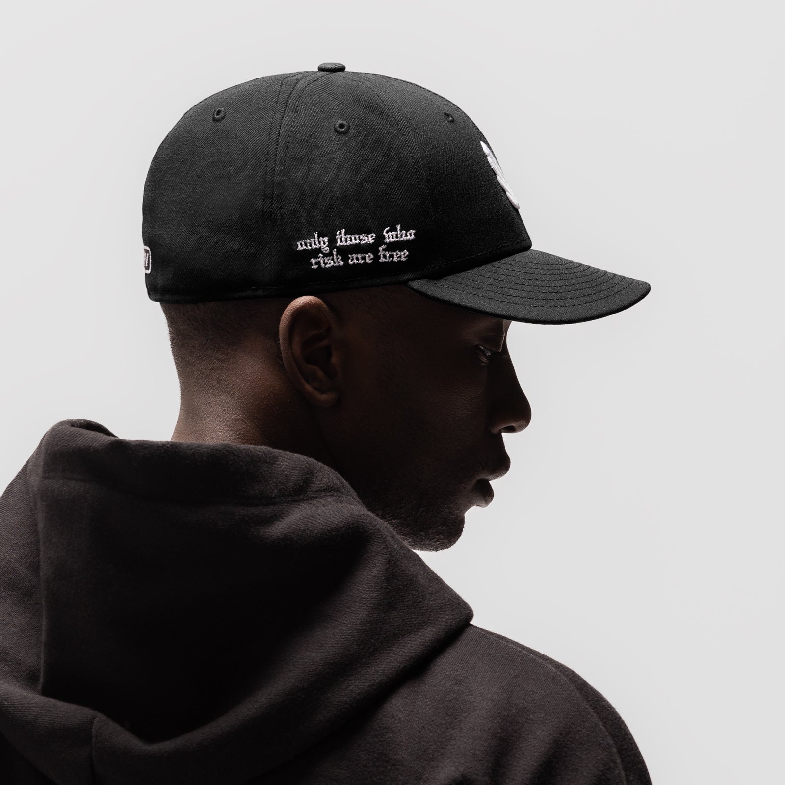New Era 59Fifty Low Profile Hat in black with white embroidered text, worn by model in profile