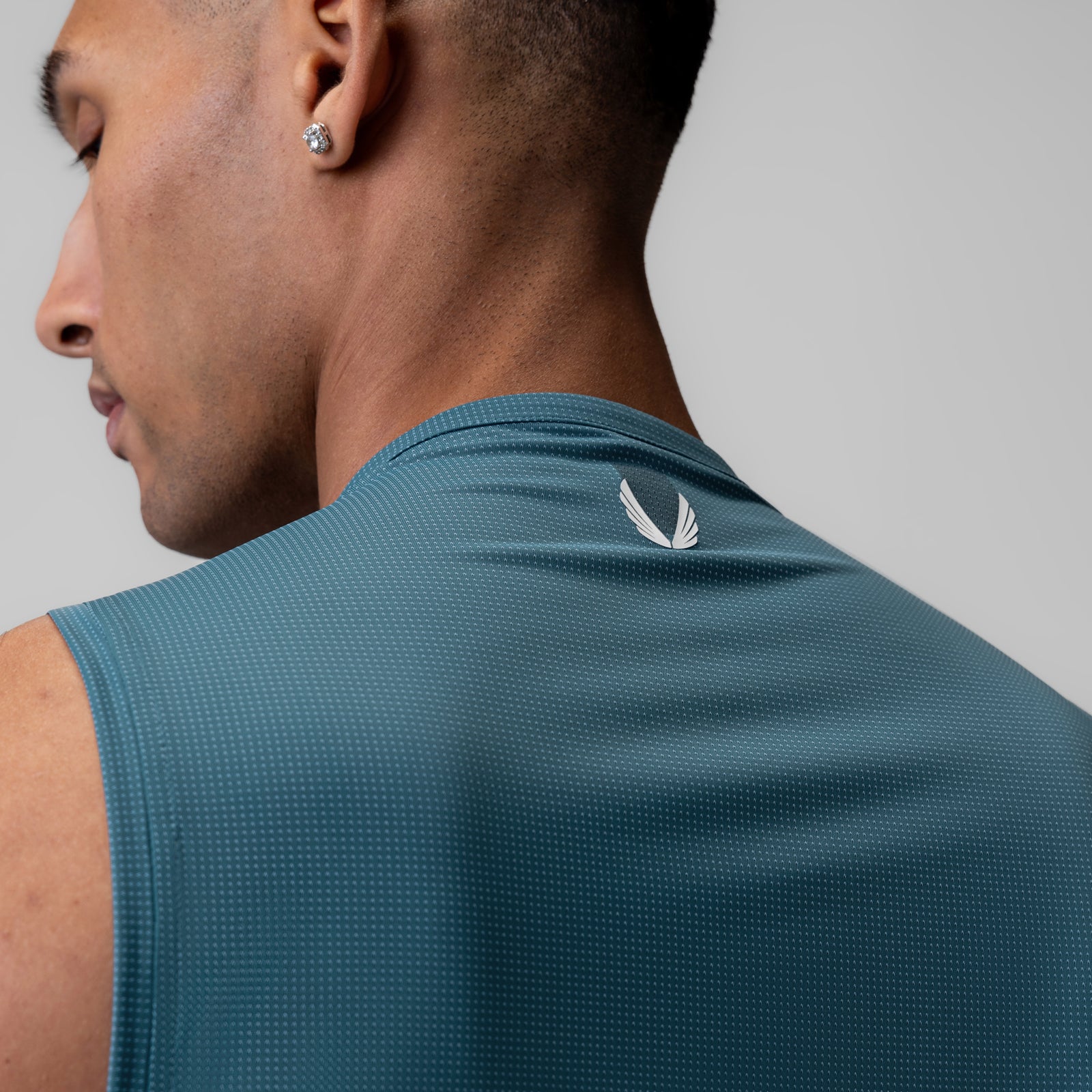 Ice-Skin™ Muscle Tank in storm blue worn by model, rear view showing feather logo