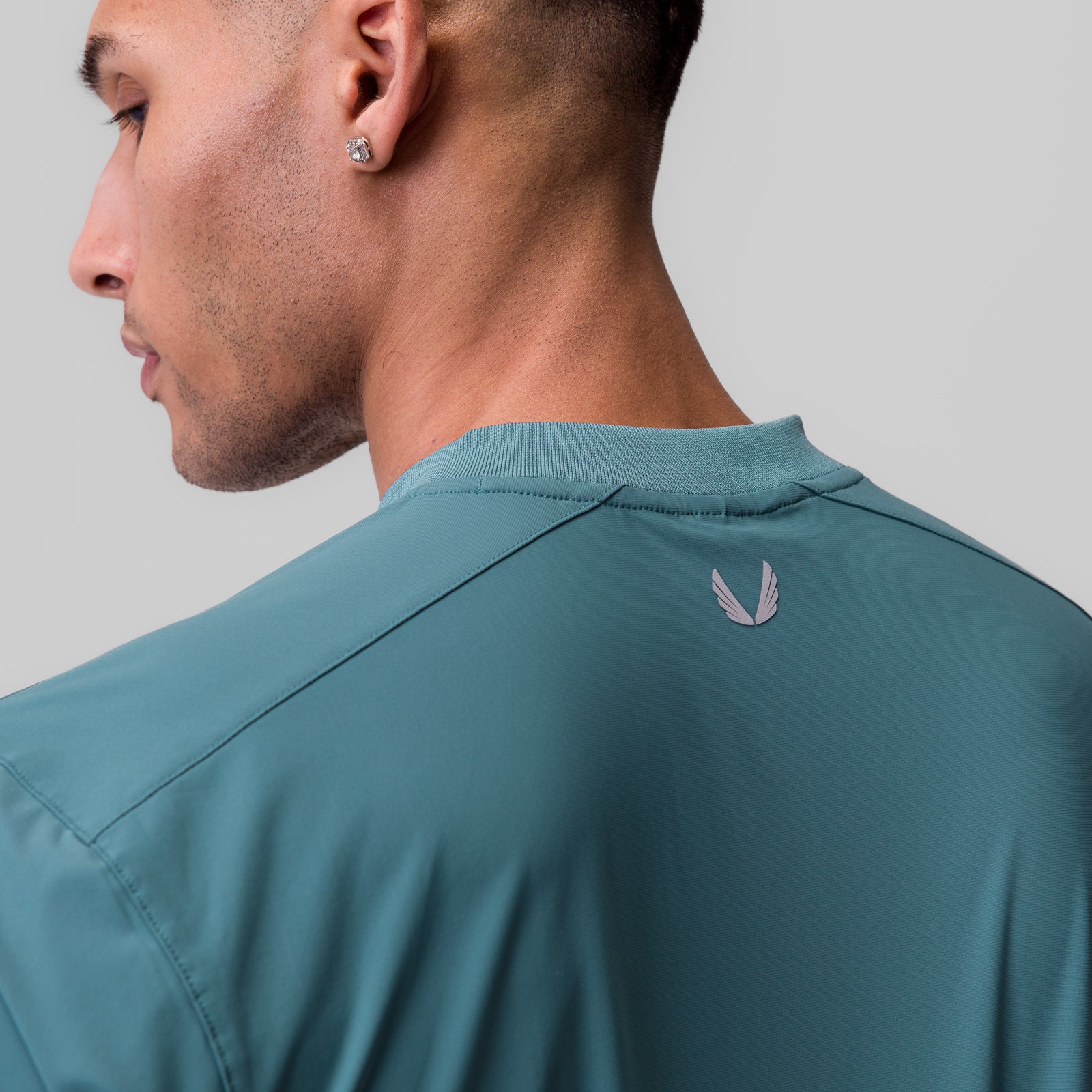 Tetra-Lite® Ice Zip Tee in Storm blue worn by model, back view showing feather logo