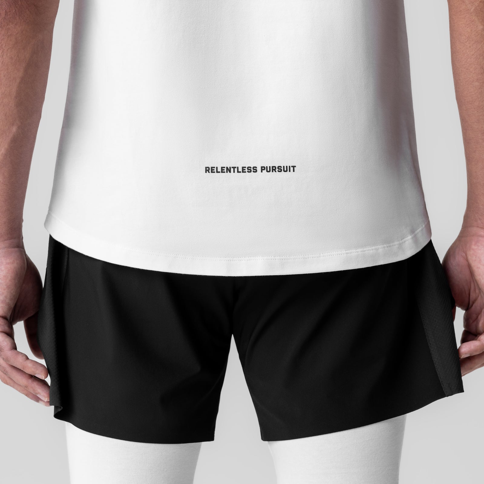 White Creora® Cotton Modal Cutoff Tank with 'Relentless Pursuit' text, worn with black shorts, back view