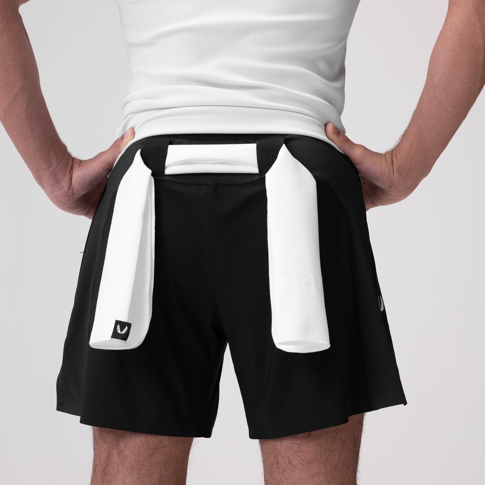 Black athletic shorts with white side pockets on model wearing white tank top, back view