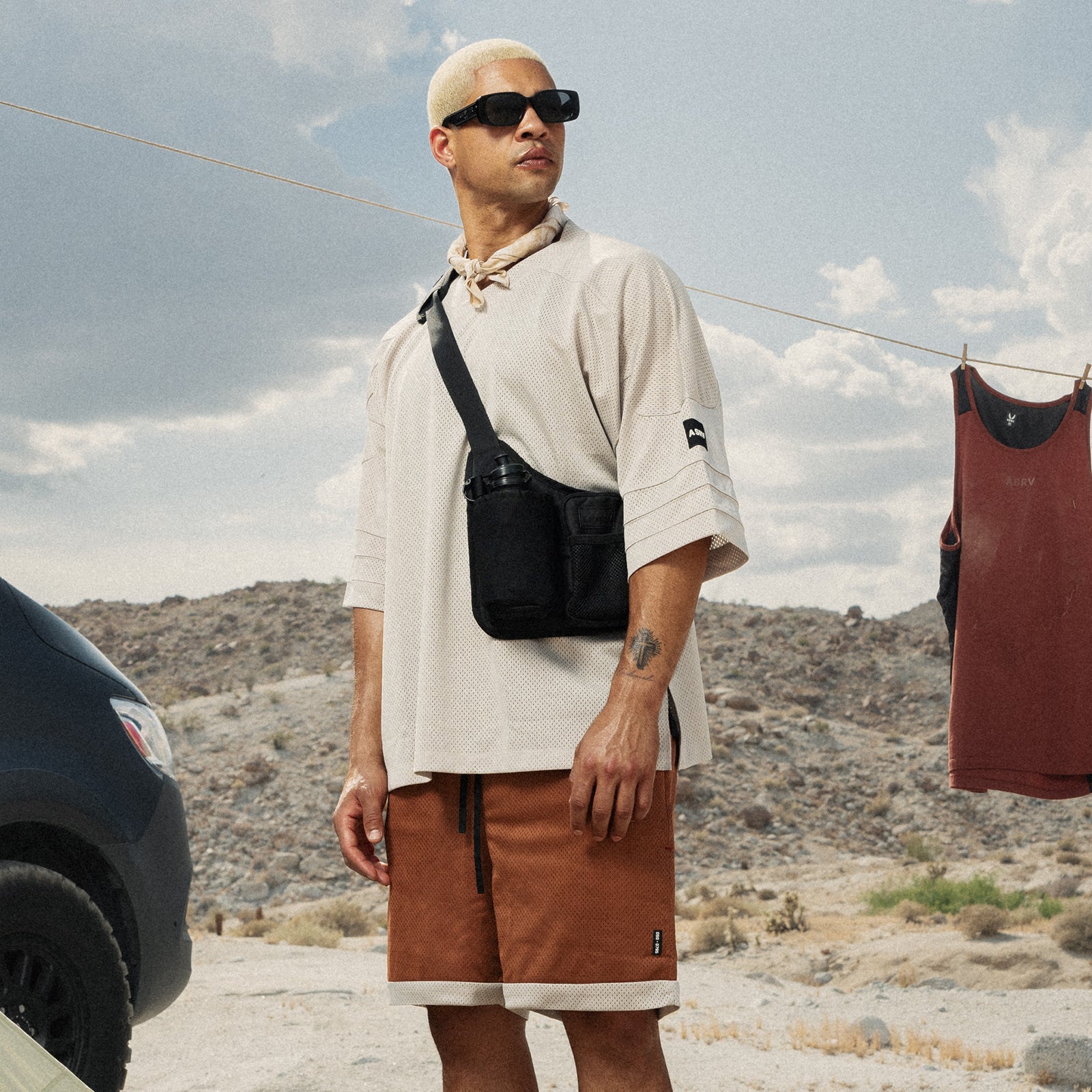 Black water bottle holster bag worn as crossbody on model in white tee and brown shorts
