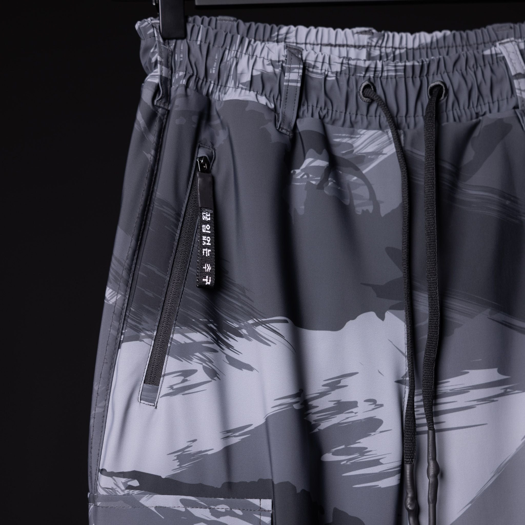 SM'20 Cargo High Rib joggers in grey camo, detail shot of drawstring and zipper pockets