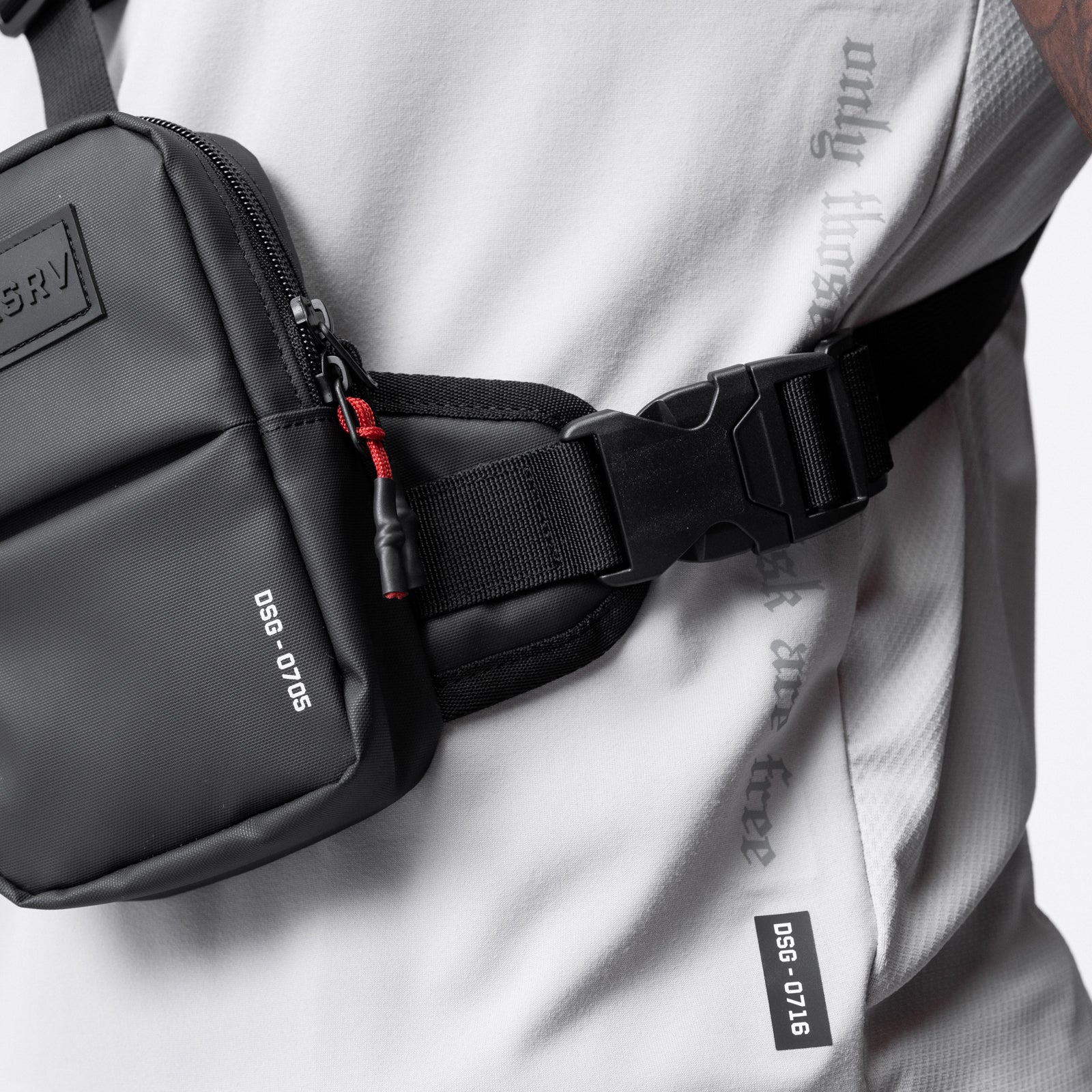 Black waterproof holster sling bag worn across chest on model in white athletic jacket