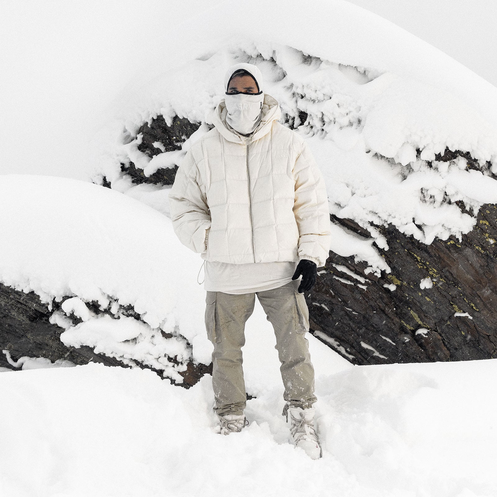 Ivory cream down puffer jacket worn by model standing in deep snow with snowy mountain backdrop